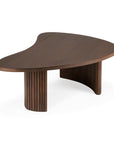 The Boomerang Coffee Table by Ethnicraft features a dark brown, FSC-certified varnished teak top with an organic silhouette and two curved, fluted legs adorned with vertical grooves.