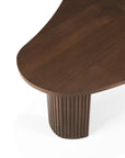 A close-up of the Ethnicraft Boomerang Coffee Table in varnished teak, showcasing its smooth, curved edges, organic silhouette, and a rounded base with vertical grooves, set against a white background.