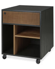 The Oscar Drawer Unit by Ethnicraft is a black rolling cabinet crafted with a solid teak wood drawer, styled with vertical grooves on the front. Inspired by classic design, it offers versatile office storage with open compartments below, divided by a shelf and partition for organized functionality.