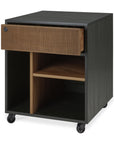 The Ethnicraft Oscar Drawer Unit - Teak - Black is a modern, box-shaped unit on wheels featuring a black frame, one solid textured teak drawer, and open compartments with vertical and horizontal wood-finished dividers.