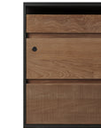 Close-up of the Ethnicraft Oscar Drawer Unit - Teak - Black, featuring three solid teak drawers with natural wood grain, a black frame, lock on the top left drawer, textured vertical lines on the bottom drawer, and wheels for mobility.