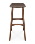 Front view of Ethnicraft’s Osso Counter Stool - Teak, showcasing a rectangular seat and four angled legs with horizontal supports. Made from FSC-certified teak, it features a smooth dark brown finish.