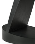 Close-up of the Oblic Side Table - Black by Ethnicraft, featuring a modern geometric design with a curved, flat vertical piece intersecting a round base. Smooth surfaces and visible wood grain emphasize its sculptural appeal.