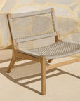 The Ethnicraft Jack Woven Outdoor Lounge Chair features a light wood frame and Italian weave beige seat and backrest, set on a sunlit patio in front of a stone wall.