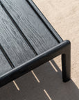 Close-up of a black wooden bench on an Ethnicraft Nomad Outdoor Rug, a textured beige indoor/outdoor rug crafted from recycled PET yarns.