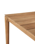 Close-up of the corner of the Ethnicraft Bok Outdoor Extendable Dining Table in natural teak, featuring a smooth slatted surface and angled legs, set against a plain white background.