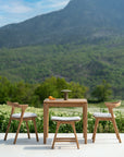 The Ethnicraft Osso Outdoor Stools with cushions are arranged on a patio overlooking greenery and mountains, surrounding a small square table topped with a lantern and oranges.