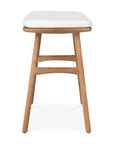 The Osso Outdoor Stool by Ethnicraft features four teak legs, a light-colored cushioned seat, and a curved support bar, shown from the front on a white background.