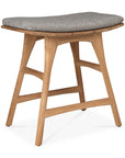 The Ethnicraft Osso Outdoor Stool with cushion features gently curved teak legs and a padded gray fabric seat, embodying minimalist Scandinavian design inspired by the Ethnicraft outdoor collection.