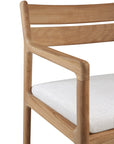A close-up of the Ethnicraft Jack Outdoor Dining Chair in solid teak with armrests and horizontal slat back, upholstered in textured outdoor fabric—blending minimalist design with classic European refinement.