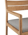 Close-up of the Ethnicraft Jack Outdoor Dining Chair - Teak (with armrest), showcasing solid teak construction and a light gray upholstered seat cushion for classic European style.