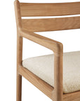 A close-up of the Ethnicraft Jack Outdoor Dining Chair - Teak, featuring a smooth solid teak frame, curved backrest and armrests, and a light-colored outdoor fabric seat.