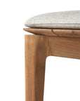 Close-up of a solid teak chair leg with a light-colored, textured cushion on top. The natural finish showcases the wood grain and joinery, echoing Ethnicrafts craftsmanship found in the Bok Outdoor Bench - Natural Teak.