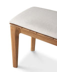A close-up of the Ethnicraft Bok Outdoor Bench - Natural Teak, crafted from solid teak with a light beige cushion, highlights the corner and two legs against a white background.