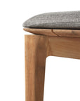 Close-up of the Bok Outdoor Bench by Ethnicraft, showcasing its solid natural teak craftsmanship and elegant wood grain, with a cushioned gray seat detail reminiscent of the brand’s signature design, set against a white background.