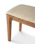 A close-up of the Ethnicraft Bok Outdoor Bench - Natural Teak, highlighting its solid teak frame and light beige textured upholstered seat, with focus on the corner and legs against a white background.