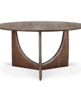 The Ethnicraft Geometric Dining Table in Brown Teak features a round wooden top, smooth dark finish, and a distinctive base of intersecting curved supports forming a half-moon design.