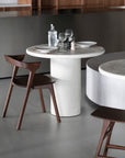 The Ethnicraft Elements Dining Table, set for two with glassware and plates, stands elegantly minimalist with two curved-back wooden chairs on a light microcement floor.