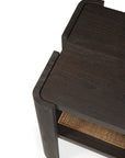 A close-up of the Ethnicraft Panel Side Table, featuring dark wood with rounded edges, a smooth top surface, and a woven cane lower shelf.