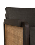 Close-up of the Ethnicraft Panel Lounge Chair in dark brown teak, featuring a wooden frame, woven cane rattan side detailing, and a dark charcoal-gray cushion for a blend of natural and contemporary style.