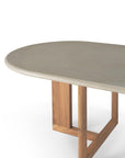 A close-up of the Ethnicraft Trestle Outdoor Dining Table features an oval light grey concrete top and geometric wooden legs, set against a white background.