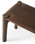 A close-up of the Ethnicraft Pi Bench in teak highlights its smooth, rounded edges and uniquely shaped corner legs. The rich teak wood grain finish reflects classic European elegance.