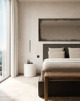 A minimalist bedroom featuring the elegant Ethnicraft Revive Bed - Grey with linen removable covers, complemented by two pillows, a wooden bench, a round white side table, and a pendant light. Floor-to-ceiling windows fill the space with natural light, while neutral tones and modern decor contribute to a serene atmosphere.