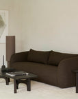 Minimalist living room with a dark brown sofa, two vintage modern furniture pieces—including an Ethnicraft Flow Side Table and a solid mahogany side table—a tall cylindrical lamp, abstract wall art, and a light textured rug on neutral-colored floor and walls.