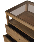 An angled top view shows the Ethnicraft Spindle Dresser - Teak, featuring a glass top and two partially open drawers, set against a white background.