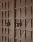 Close-up of Ethnicrafts Sono Cupboard shows two solid teak doors with hand-carved, three-dimensional geometric diamond panels and round metallic knobs, all finished in a rich, dark brown.