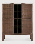 The Ethnicraft Sono Cupboard is a tall solid teak cabinet with hand-carved geometric doors, partially open to show four shelves. It stands on four simple straight legs.
