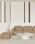 A minimalist living room with the Ethnicraft Bulky Modular Sofa in Light Sepia, paired with a matching ottoman, round white coffee table, modern white table lamp, decorative wall panels, and a light textured rug.