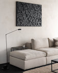 A modern living room with the Ethnicraft Mellow Modular Sofa in Off White, a black side table with candle, sleek black floor lamp, and abstract black wall art on an off-white textured wall. The minimalist decor highlights neutral tones.