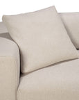 The Ethnicraft Mellow Cushion, a beige memory foam throw pillow, rests against the backrest of a matching beige fabric sofa, with its cushion and armrest visible on a white background.