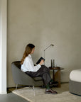A person sits in a gray Ethnicraft Barrow Lounge Chair - Paon, writing in a notebook next to a small side table.