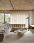 Minimalist living room featuring the Ethnicraft N701 Modular Sofa in ecru eco fabric, an oval coffee table, floor lamp, large window with sheer curtains, and wooden ceiling. The space feels bright and serene.