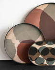 The Ethnicraft Overlapping Dots Tray (Round/Large) features an abstract pattern in muted tones of brown, green, beige, and black. Its rounded shape and modern design add artistic flair to any space, inspired by Translucent Silhouettes.