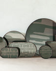 Second Nature Trays by Ethnicraft feature minimalist geometric patterns in earthy green, gray, and neutrals. Hand-printed glass details highlight their unique design against a light wall on a white surface.