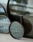 A close-up of Ethnicrafts Second Nature Tray collection, featuring round and rectangular trays with abstract green and white patterns on hand-printed glass, elegantly displayed on a light surface under soft lighting.