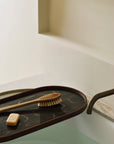 The Ethnicraft Second Nature Tray holds a natural bristle brush and soap above a water-filled bathtub, positioned by a wall with a brass faucet.
