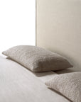A close-up of the Ethnicraft Revive Bed - Sand highlights its beige fabric headboard and two textured beige pillows with 100% linen covers atop a light-colored bedsheet.