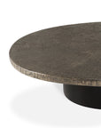 A close-up of the Ethnicraft Slice Coffee Table, featuring a modern round design with a textured, dark stone-like top and natural mineral finish on a black cylindrical base, shown against a white background.
