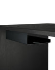 Close-up of a modern black desk with the Ethnicraft Metal Cable Tray, inspired by classic European design, featuring a built-in rectangular metal shelf for organizing cables and holding small items.