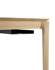 Close-up of a modern wooden table with clean, angular lines and an Ethnicraft Metal Cable Tray in black under the tabletop, showcasing light natural wood grain and refined European design for under-desk cable organization.