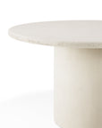 The Elements Dining Table by Ethnicraft features a minimalist round design with a textured off-white microcement surface and a thick cylindrical base, showcased against a plain white background.