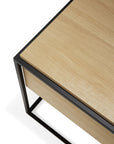 A close-up of the Ethnicraft Monolit Nightstand in oak highlights its light European oak surface and sleek black metal frame, showcasing fine corner and edge details—a striking example of modern design.