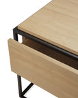 A close-up of the Ethnicraft Monolit Nightstand - Oak, crafted from European oak, with a partially open drawer and a sleek black metal frame.