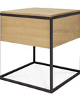 The Ethnicraft Monolit Nightstand - Oak features a light European oak cube top and sides, supported by an open black metal frame for a minimalist, contemporary look that blends classic European refinement with industrial style.