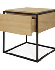 The Monolit Nightstand - Oak by Ethnicraft is a modern square side table in European oak, with a black metal frame and open drawer, blending minimalist design and classic European refinement.