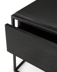 Close-up of the Ethnicraft Monolit Nightstand in black oak featuring a partially open drawer and minimalist metal frame, highlighting classic European refinement.